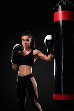 Kadın Boxer siyah arka planda boks torbası ile eldiven mücadele. Boks ve fitness konsepti.