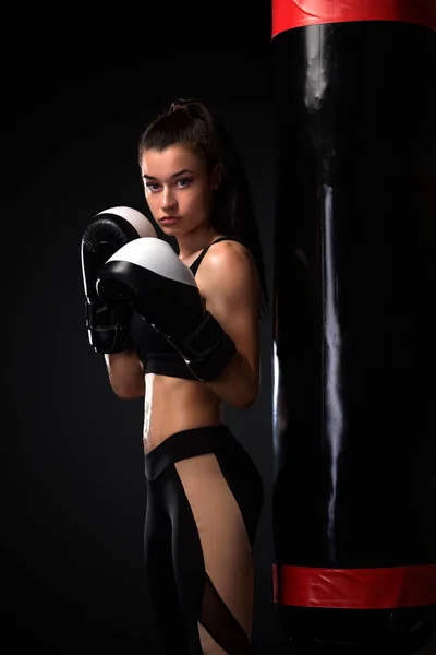 Woman boxer fighting in gloves with boxing punching bag on black background. Boxing and fitness concept.
