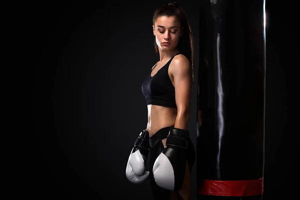Mulher boxeador lutando em luvas com boxe saco de perfuração no fundo preto. Conceito de boxe e fitness . — Fotografia de Stock