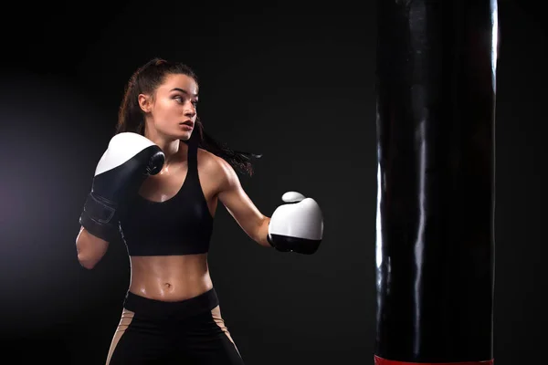Boxer donna che lotta in guanti con sacco da boxe su sfondo nero. Boxe e fitness concept . — Foto Stock