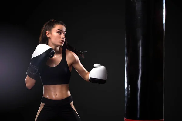 Mulher boxeador lutando em luvas com boxe saco de perfuração no fundo preto. Conceito de boxe e fitness . — Fotografia de Stock