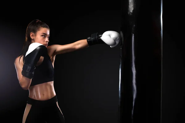 Boxer donna che lotta in guanti con sacco da boxe su sfondo nero. Boxe e fitness concept . — Foto Stock