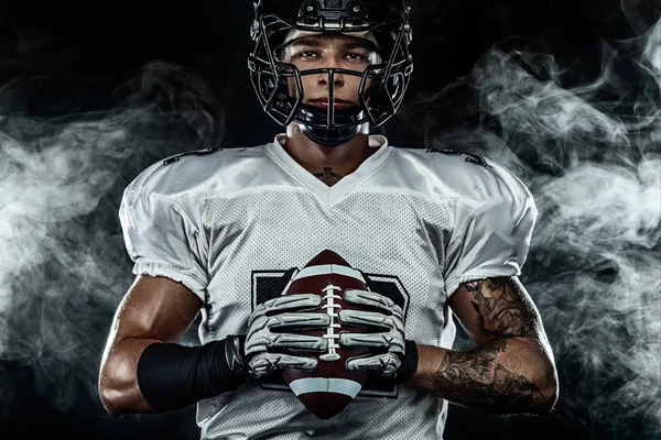 アメリカンフットボール選手、煙と黒い背景にヘルメットのスポーツマン。スポーツとモチベーションの壁紙. — ストック写真
