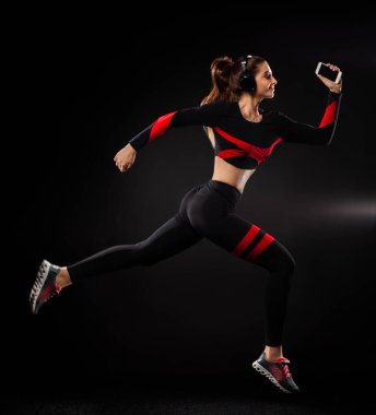 Güçlü atletik kadın koşucu, siyah arka planda koşuyor spor giyim ve kulaklık takıyor. Spor ve spor motivasyonu. Çalıştırıcı kavramı.