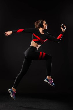 Güçlü atletik kadın koşucu, siyah arka planda koşuyor spor giyim ve kulaklık takıyor. Spor ve spor motivasyonu. Çalıştırıcı kavramı.