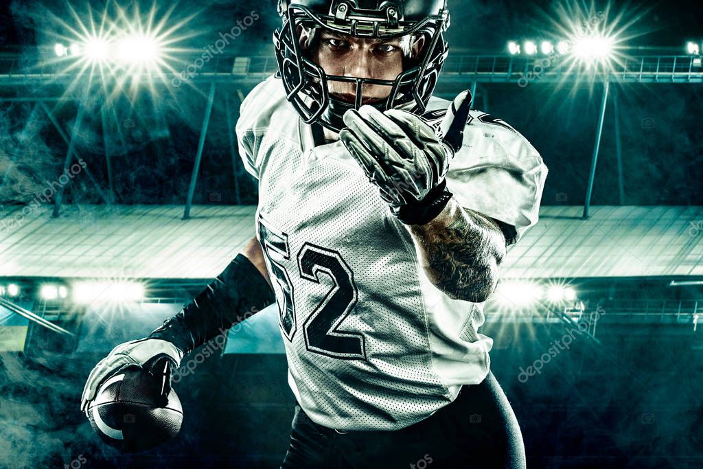 American football player. Sportsman with ball in helmet on stadium in action. Sport wallpaper. Closeup portrait.