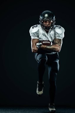 Kask lı Amerikalı futbolcu siyah arka planda hareket halinde. Spor ve motivasyon duvar kağıdı. Takım sporları,