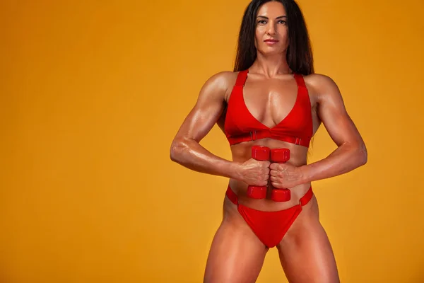 Güçlü kas vücut geliştirmeci atletik kadın sarı arka plan üzerinde dumbbells ile kasları pompalama. Bireysel spor rekreasyon. — Stok fotoğraf