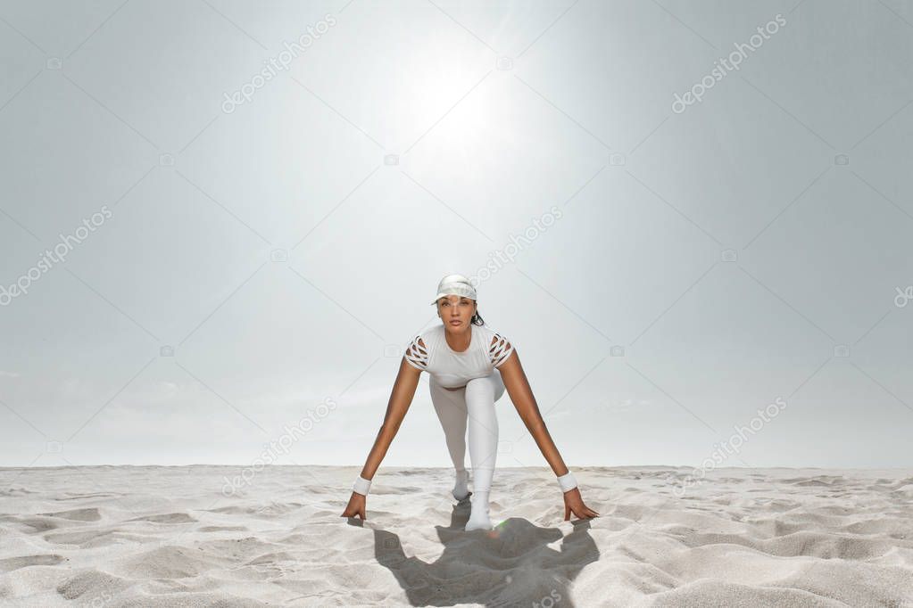 Fit woman sprinter, start running at the desert wearing in white sportswear. Fitness and sport motivation. Runner concept with copy space.