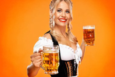 Genç seksi oktoberfest kız garson, geleneksel Bavyera veya Alman dirndl giyen, sarı arka plan izole içki ile büyük bira kupaları hizmet.
