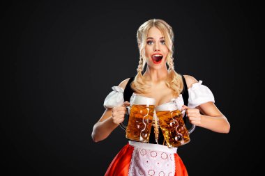 Genç seksi oktoberfest kız garson, geleneksel Bavyera veya Alman dirndl giyen, siyah arka plan izole içki ile iki büyük bira kupaları hizmet.