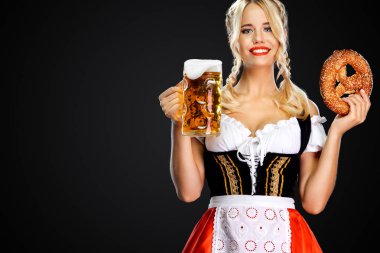 Gülümseyen genç seksi Oktoberfest kız garson, geleneksel Bavyera veya Alman dirndl giyen, içki ve bretzel ile büyük bira kupaları hizmet, siyah arka plan üzerinde izole.