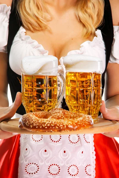 Close-up van jonge sexy Oktoberfest meisje serveerster, het dragen van een traditionele Beierse of Duitse Dirndl, serveren twee grote bier mokken met drankje en bretzel. — Stockfoto