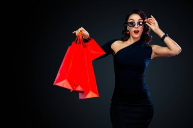 Dükkan için Black Friday satış konsepti. Koyu arka plan üzerinde izole kırmızı çanta tutan güneş gözlüğü alışveriş kadın.