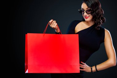 Dükkan için Black Friday satış konsepti. Koyu arka plan üzerinde izole kırmızı çanta tutan güneş gözlüğü alışveriş kadın.