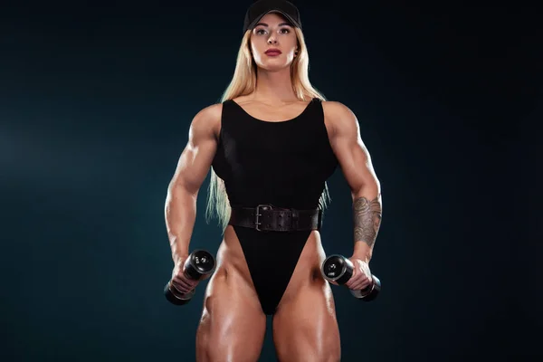 Fuerte mujer atlética culturista con mancuernas sobre fondo oscuro vistiendo en ropa deportiva. Fitness y motivación deportiva . — Foto de Stock