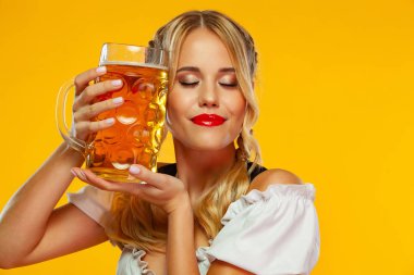 Genç seksi Oktoberfest kız garson, sarı arka plan izole büyük bira kupa ile geleneksel Bavyera veya Alman dirndl giyiyor. Kadın bira seviyorum.