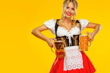 Vay canına duygu. Genç seksi Oktoberfest kız garson, geleneksel Bavyera veya Alman dirndl giyen, sarı arka plan izole içki ile büyük bira kupaları hizmet.
