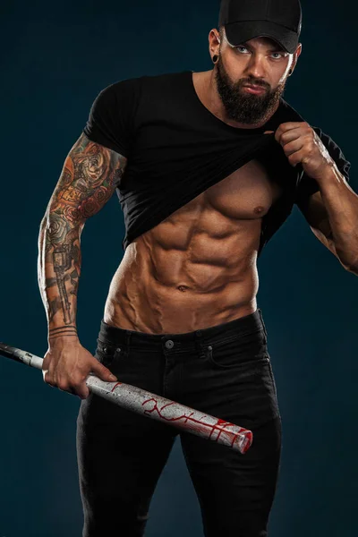 Сильный и здоровый бодибилдер с бейсбольной битой показывает мышцы живота под футболкой. Спортивный мускулистый спортсмен. Концепция спорта и фитнеса. Мужская мода . — стоковое фото
