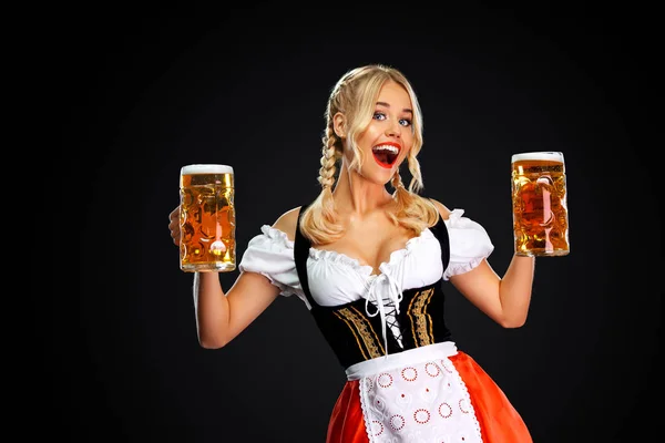Gelukkig sexy Oktoberfest meisje serveerster, het dragen van een traditionele Beierse of Duitse Dirndl, serveren twee grote bier mokken met drankje geïsoleerd op zwarte achtergrond. — Stockfoto