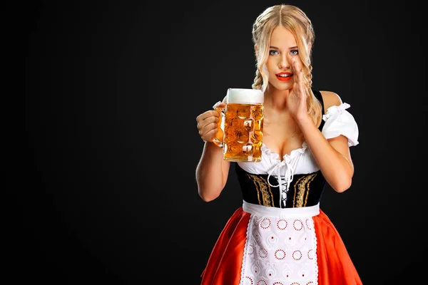Sexy servírka, která nosí tradiční bavorskou nebo německou dirndl, podává velký pivní džbánek s nápojem izolovanými na černém pozadí. Žena má tajemství. — Stock fotografie