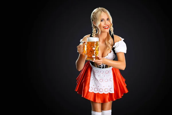 Sorrindo jovem sexy oktoberfest menina garçonete, vestindo um tradicional bávaro ou alemão dirndl, servindo caneca de cerveja grande com bebida isolada no fundo preto . — Fotografia de Stock
