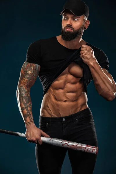 Сильный и здоровый бодибилдер с бейсбольной битой показывает мышцы живота под футболкой. Спортивный мускулистый спортсмен. Концепция спорта и фитнеса. Мужская мода . — стоковое фото