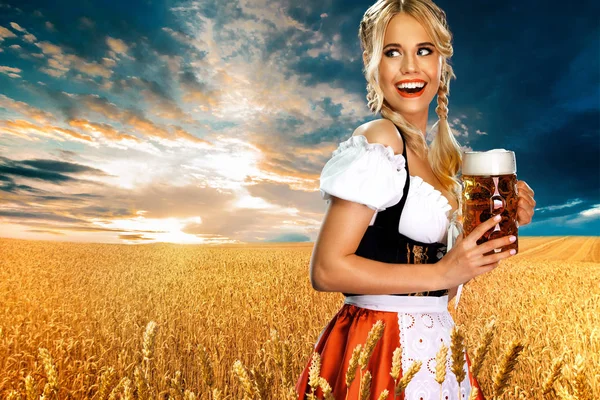 Mosolygós fiatal szexi Oktoberfest lány pincérnő, fárasztó egy hagyományos bajor vagy német Dirndl, szolgáló nagy sörösbögre itallal kültéri. Nő mutatott bal látszó. — Stock Fotó