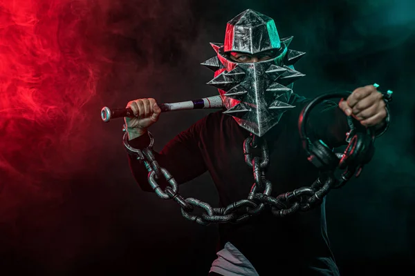 Hombre misterioso en un casco con un murciélago y cadenas en ropa negra. Libro de fantasía o juego de ordenador concepto de portada en la fiesta disco de Halloween . — Foto de Stock