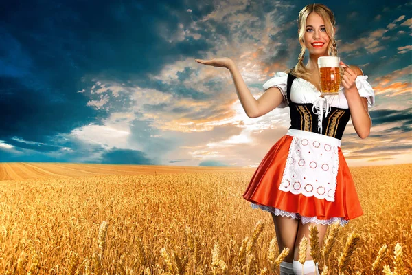 Lächelnde sexy Oktoberfestkellnerin, die ein traditionelles bayerisches oder deutsches Dirndl trägt und zwei große Bierkrüge mit Drink im Freien serviert. Frau zeigt nach links. — Stockfoto