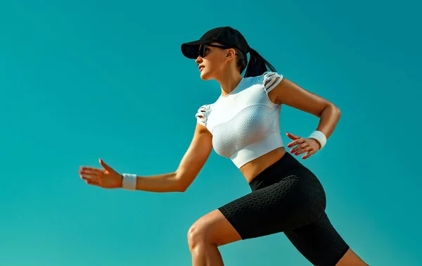 Sportif genç kadın ve gökyüzü arka planda çalışan uygun atlet koşucu. Sağlıklı bir yaşam tarzı ve spor kavramı. Siyah beyaz spor giyimli kadın. — Stok fotoğraf