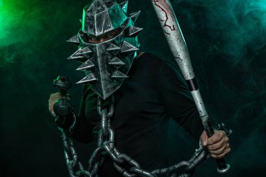 Kasklı, sopalı ve siyah giyimli zincirli gizemli bir adam. Halloween disko parti fantasy kitap veya bilgisayar oyunu kapak konsepti.