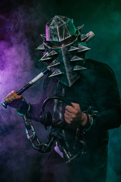 黒い服を着たバットと鎖を持ったヘルメットの謎の男。ハロウィーンディスコパーティーでファンタジーブックやコンピュータゲームカバーの概念. — ストック写真