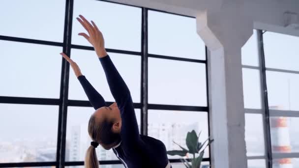Yoga binnen. Sport recreatie. Mooie jonge vrouw in yoga asana voor beginners. Individuele sporten. Kamer met groot panoramisch raam. — Stockvideo