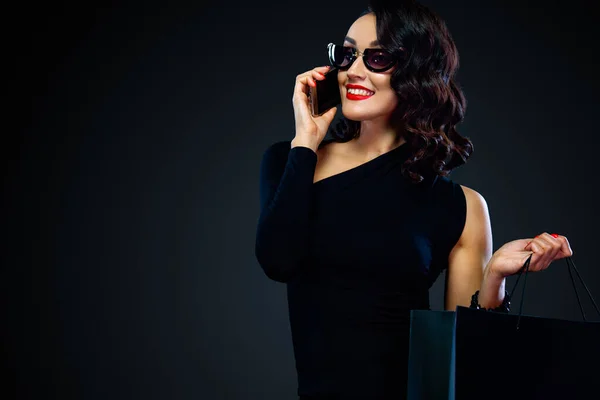 Shopping su Venerdì nero e Cyber Lunedi. Concetto di vendita per negozi. Donna che tiene la borsa e chiama al telefono, isolata su sfondo scuro — Foto Stock