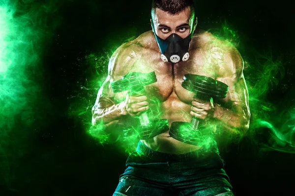 Αθλητής με πράσινα ενεργειακά φώτα. Μυώδης νεαρός αθλητικός τύπος, bodybuilder σε μάσκα κατάρτισης. Γυμναστική με αλτήρα στο γυμναστήριο — Φωτογραφία Αρχείου