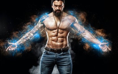 Mavi enerji lambaları içinde vücut geliştiren bir sporcu. Dövmeli kot pantolon giymiş yakışıklı bir adam. Siyah arka planda izole edilmiş spor ve moda kavramı.
