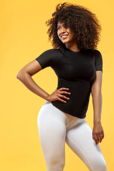 Sorrindo mulher atlética forte com pele preta e cabelo encaracolado, fazendo exercício no fundo amarelo vestindo sportswear. Aptidão e motivação desportiva . — Fotografia de Stock