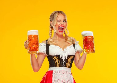 Geleneksel bir Bavyera ya da Alman dirndl giyip sarı arka planda izole edilmiş büyük bira bardakları servis eden genç seksi Ekim Festivali kız garsonu. Sola bakan kadın.