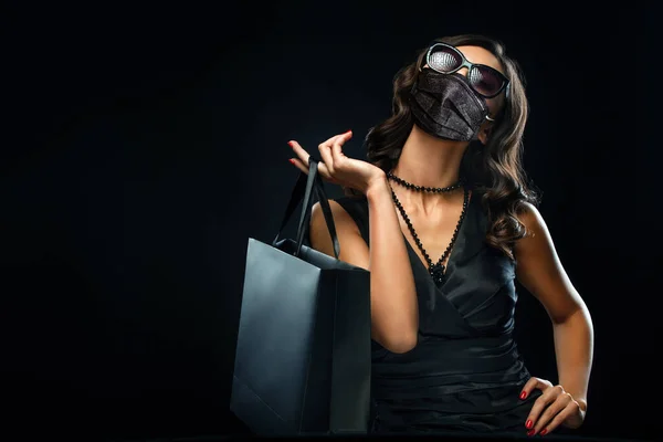 검은 금요일 판매 개념은 2020 년 코로나 바이러스가 유행 한 시기이다. 휴일에 검은 배경에서 분리 된 회색 가방을 들고 의료용 마스크를 쓰고 쇼핑하는 여성. — 스톡 사진