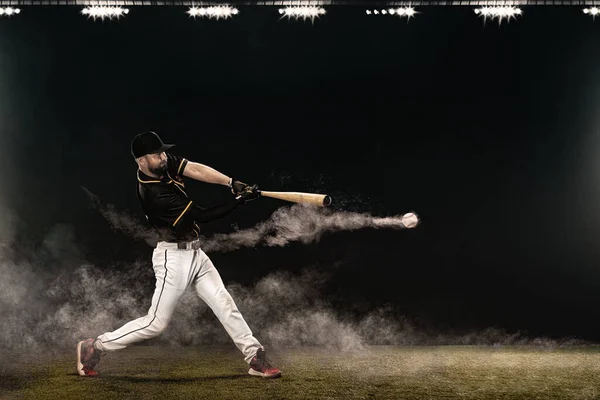Jogador de beisebol com morcego a dar uma tacada na grande arena. Ballplayer no fundo escuro em ação. — Fotografia de Stock