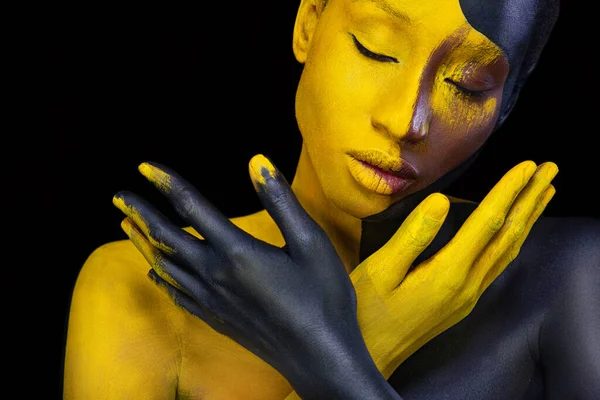 Arcművészet. Nő, fekete és sárga testfestékkel. Fiatal afrikai lány színes testfestékkel. Egy csodálatos modell sárga sminkkel. Szoros arc. — Stock Fotó