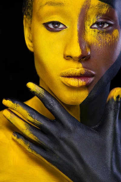 Cara de arte. Mujer con pintura corporal negra y amarilla. Chica africana joven con colorido bodypaint. Un modelo increíble con maquillaje amarillo. Cara de primer plano. —  Fotos de Stock