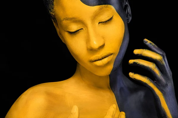 Ansiktskonst. Kvinna med svart och gul kroppsfärg. Ung afrikansk flicka med färgglad kroppsfärg. En fantastisk modell med gul makeup. Närbild ansikte. — Stockfoto