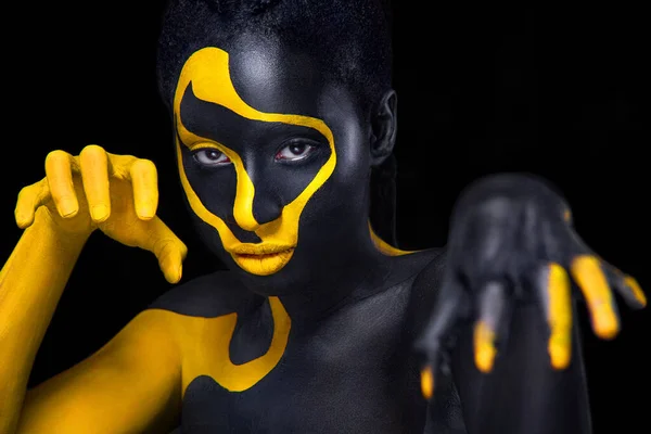 Face art. Woman with black and yellow body paint. Young african girl with colorful bodypaint. An amazing model with yellow makeup. Closeup face.