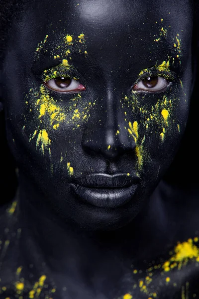 Mulher com tinta preta. Jovem menina africana alegre com pintura corporal arte. Um modelo incrível com maquiagem amarela. Cara fechada. — Fotografia de Stock