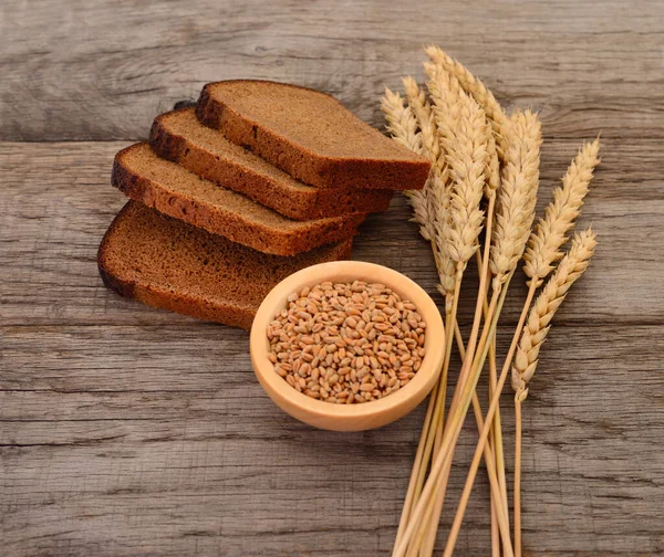 Wheat grains in a wooden bowl, wheat ears and bread.