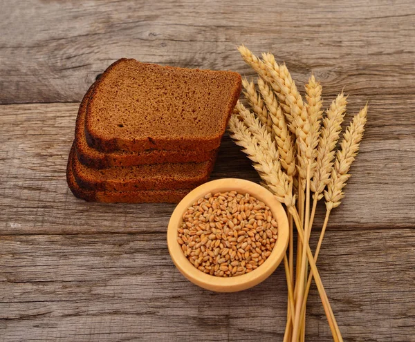 Wheat grains in a wooden bowl, wheat ears and bread.