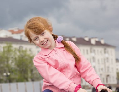 Neşeli Kızıl saçlı kız portresi. Kız evleri ve fırtınalı bir gökyüzü arka plan üzerinde.