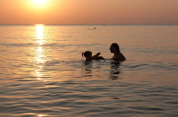 Deniz on Sunset. Bir ayar güneş ışınlarının denizde oynayan bebek ile anne siluetleri
